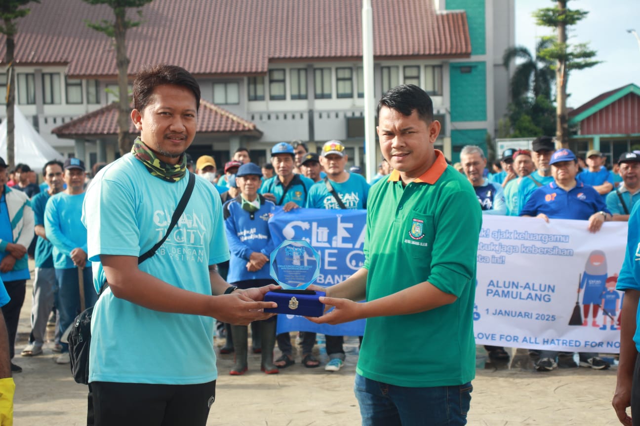 Ketua Pelaksana Clean the City di Alun-alun Pamulang, Anggi Arisandi (kiri) menyerahkan cenderamata ke perwakilan DLH Kota Tangsel. (tangselpos.id)