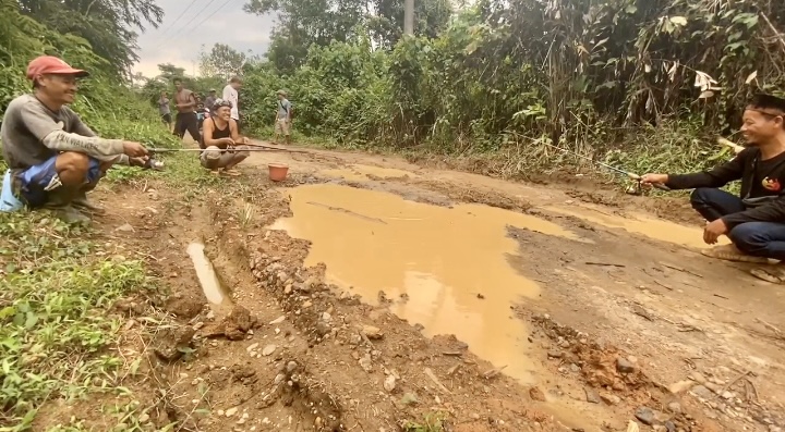 Warga Mancing Ikan Di Jalan Rusak Sejumlah warga di Kampung Pasirbinglu, Desa Jayasari, Kecamatan Cimarga, Kabupaten Lebak, sedang mancing ikan di tengah jalan, Minggu (22/6).